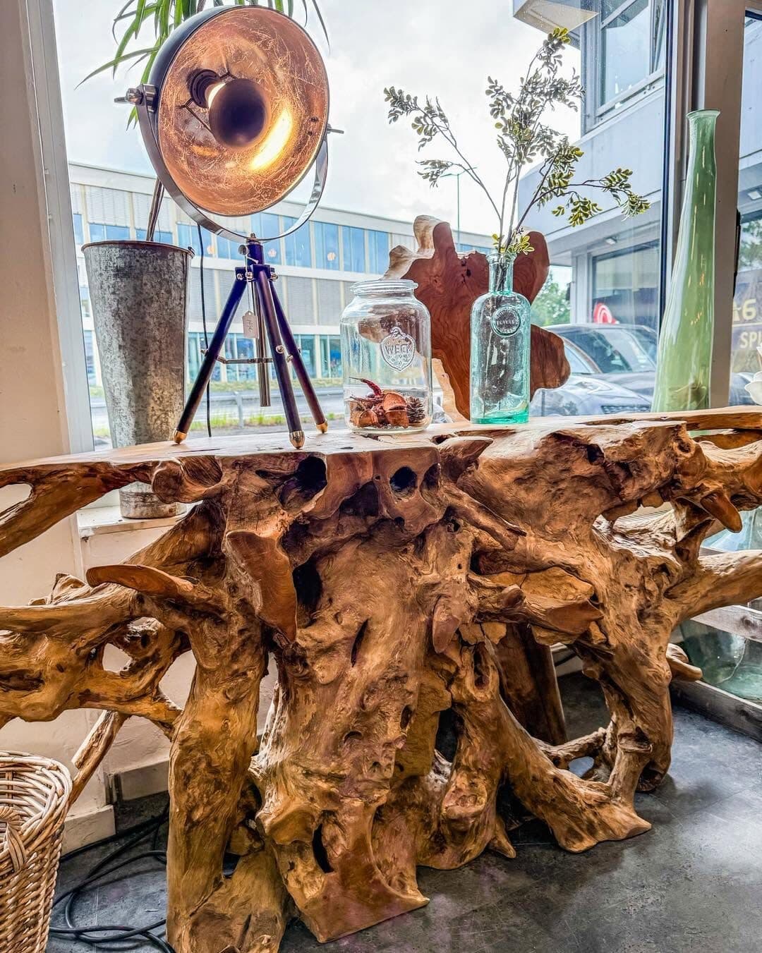 Console table made from a solid teak root with a light top, vases and a lamp on it, the shop window behind