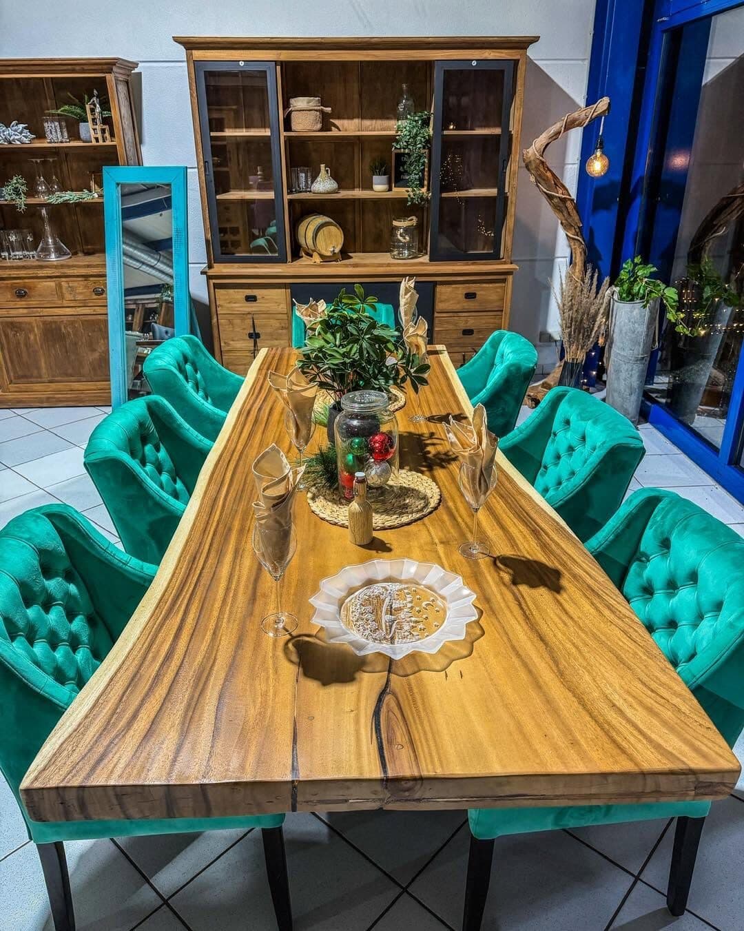 Long Suar wood dining table with a natural live edge, laid for dinner and surrounded by green velvet chairs
