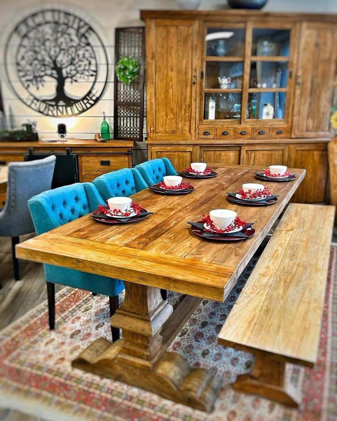 Solid teak refectory table with a trestle base and a matching bench, the Exclusive Living Furniture logo on the wall behind