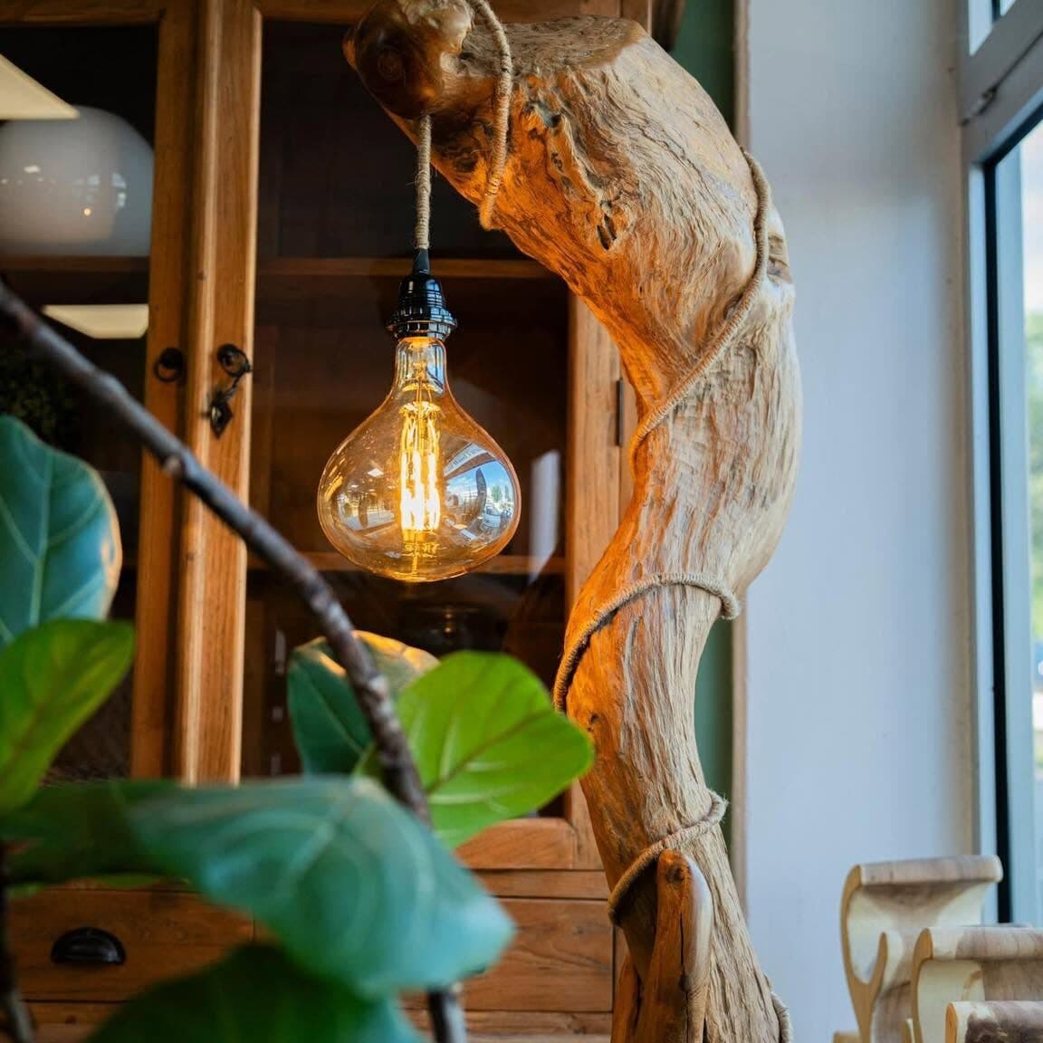 Floor lamp made from a curved piece of driftwood with a glowing Edison bulb hanging from a rope
