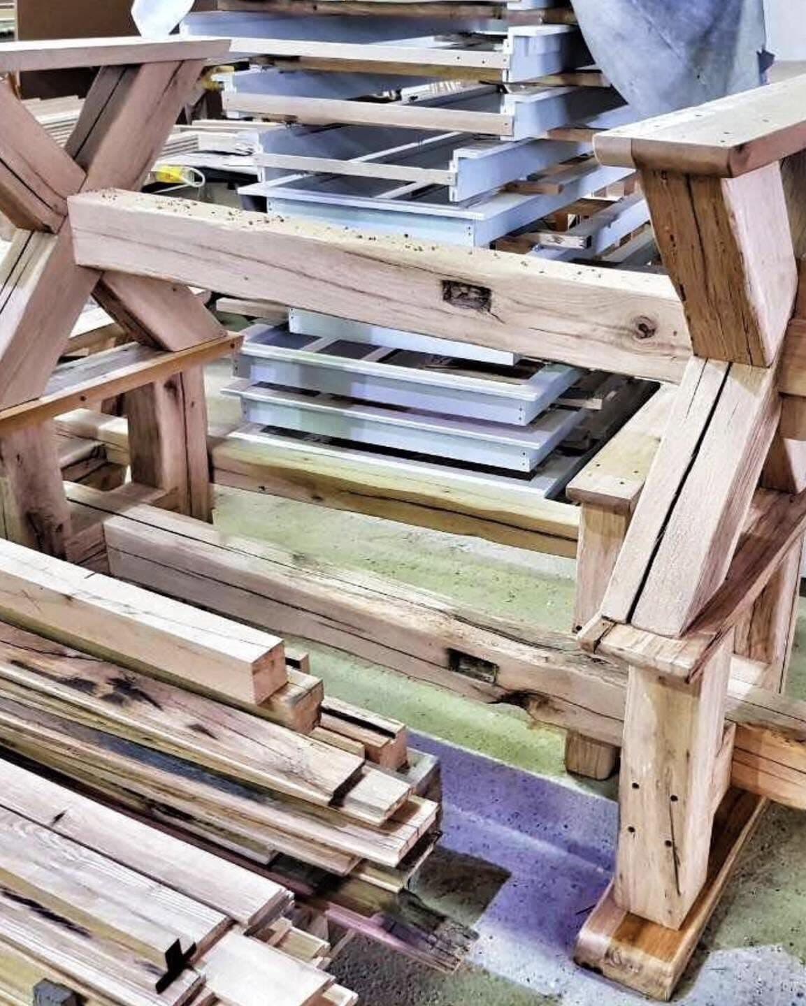 Solid wood table frame in the workshop, its braces joined with visible wooden tenons, stacked boards in front