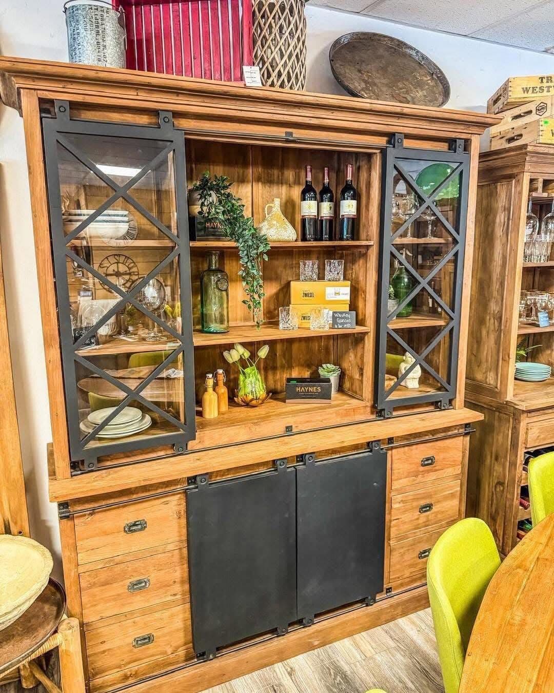 Wooden display cabinet with black metal bracing and sliding doors in industrial style, glasses and wine bottles on its shelves