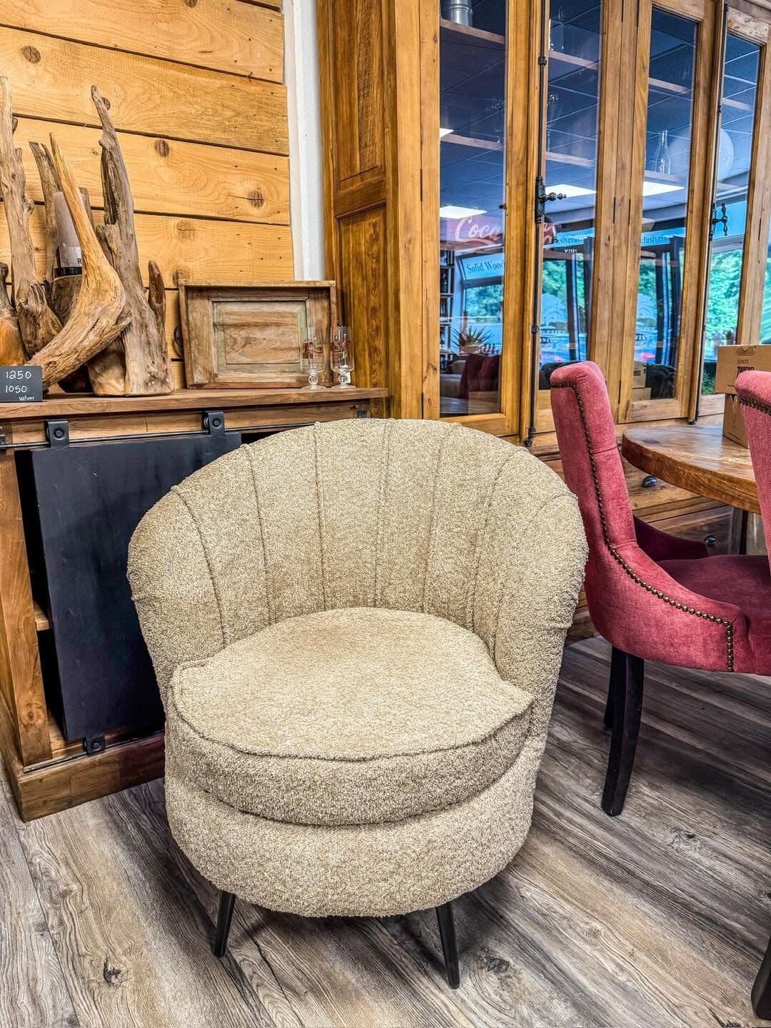 Round armchair in cream bouclé fabric on black metal legs in front of a wooden wall