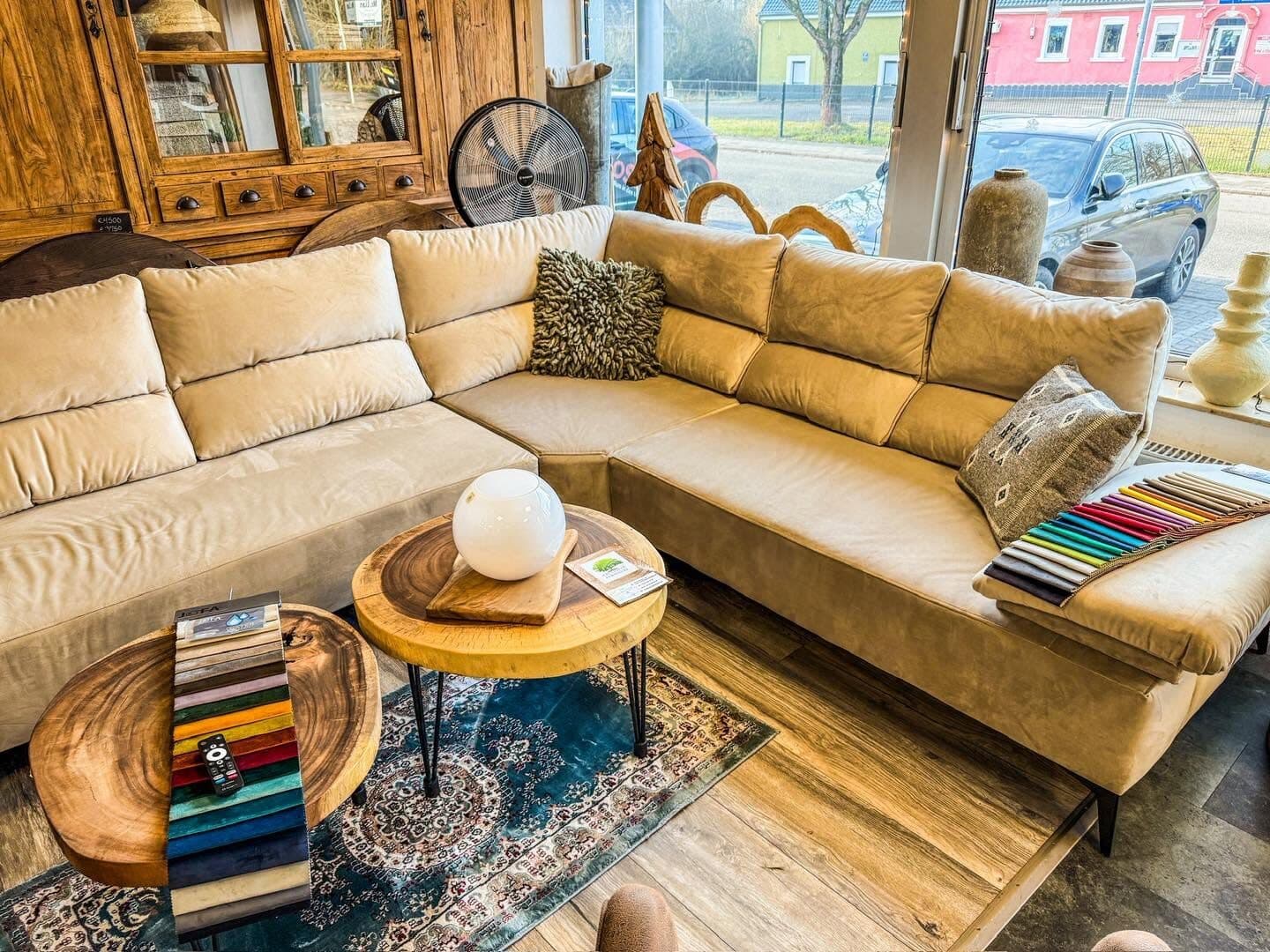 Beige suede corner sofa in the showroom, two round tree-slice coffee tables in front of it and a window onto the street behind
