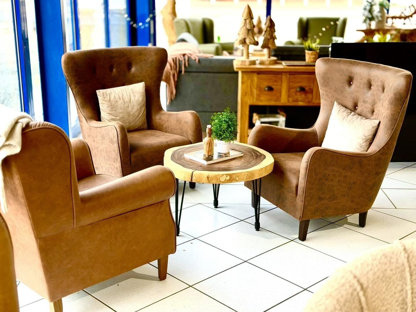 Three brown leather wing chairs around a round coffee table made from a tree slice